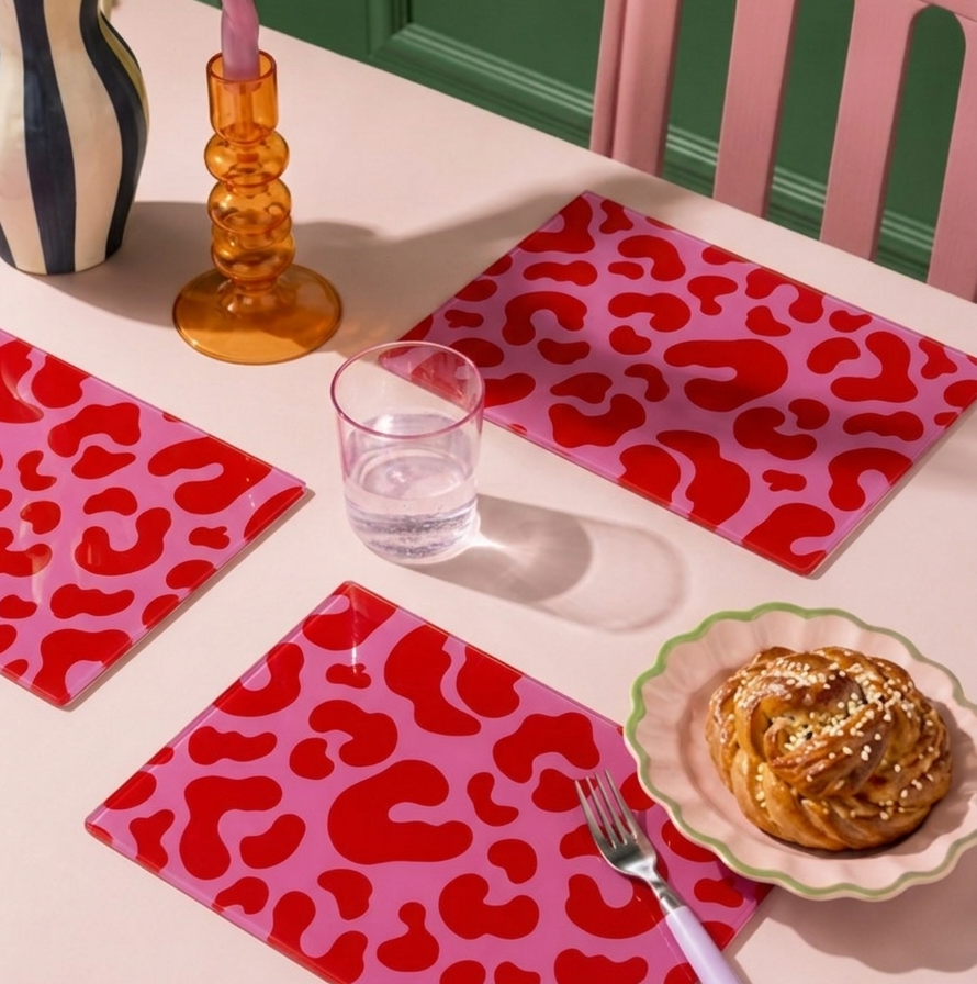 Table setting with pink and red leopard print glass placemats, a glass of water, a pastry, and a fork 