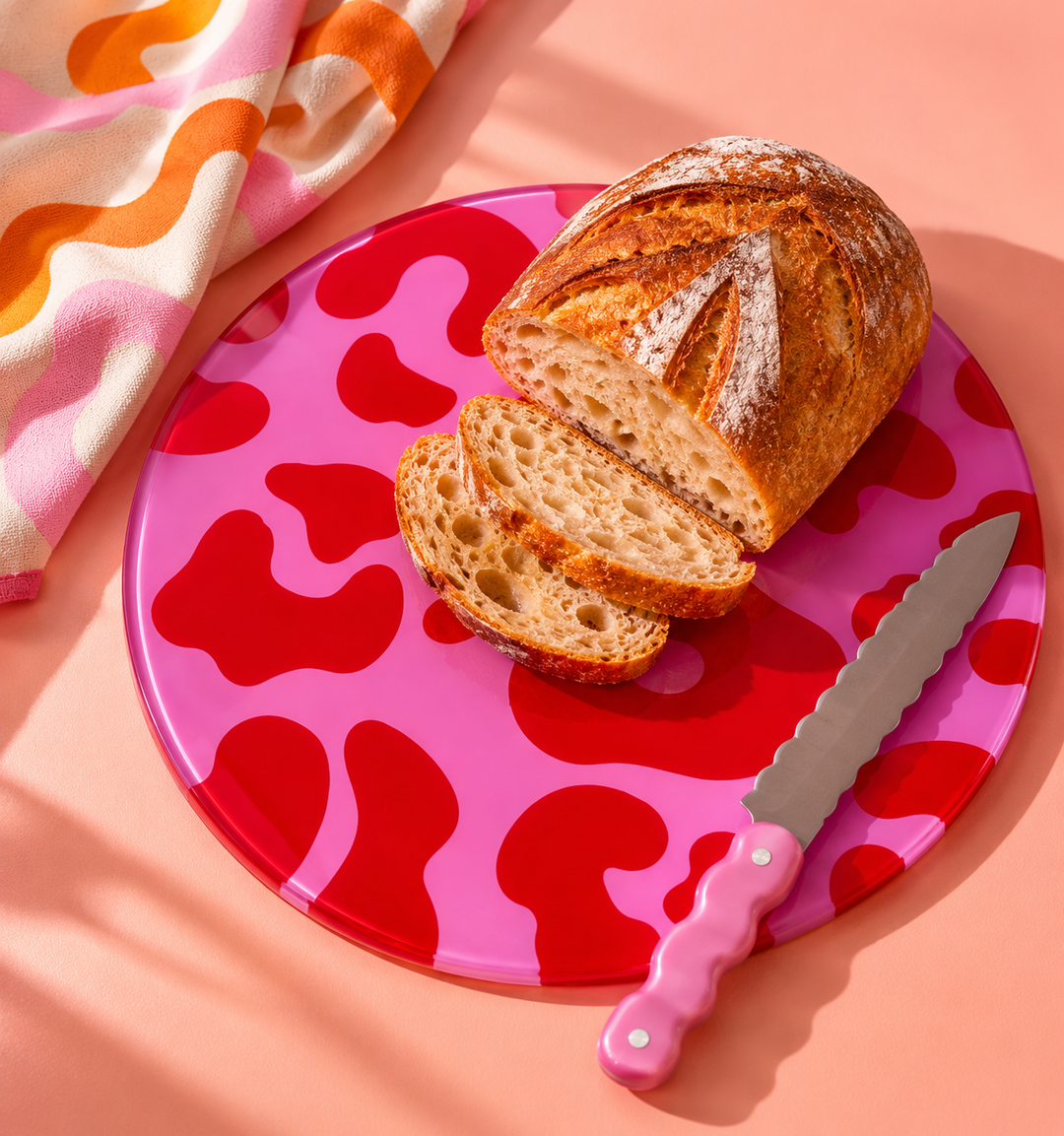 Pink Red Leopard print round glass worktop saver with bread on top and a pink knife against a peach background 