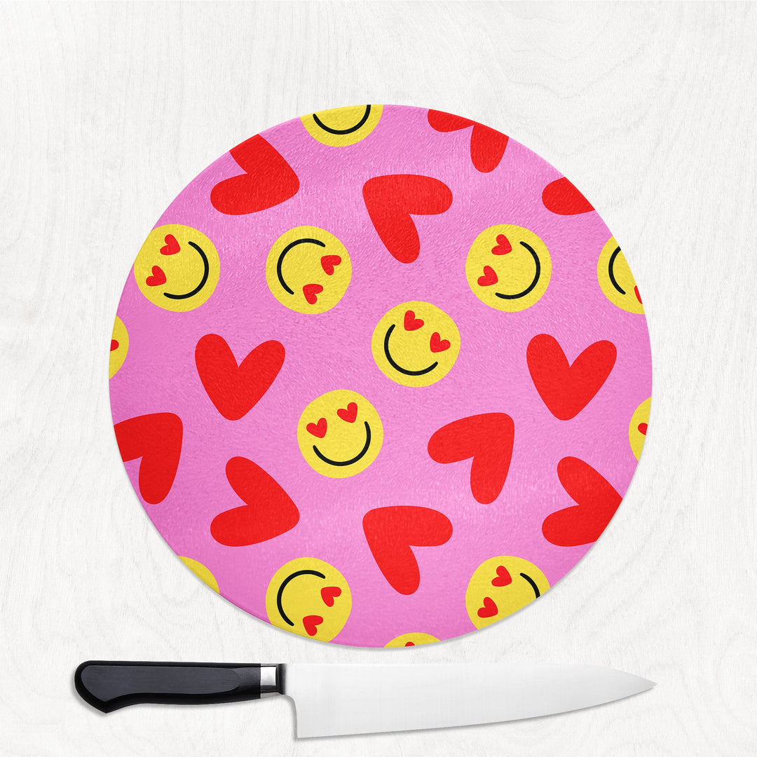Pink cutting board with smiley face and heart patterns next to a knife on a white background