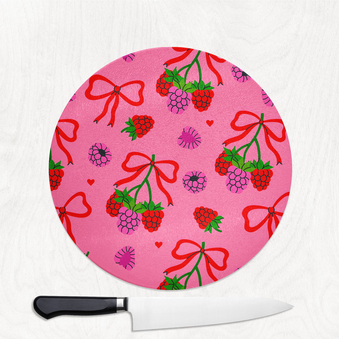 Round pink cutting board with red bows and berries design on a white background