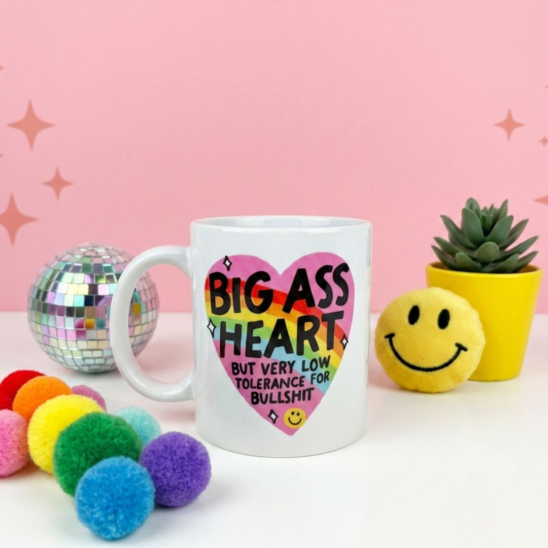 Mug with colorful text design on a pink background with decorative items.