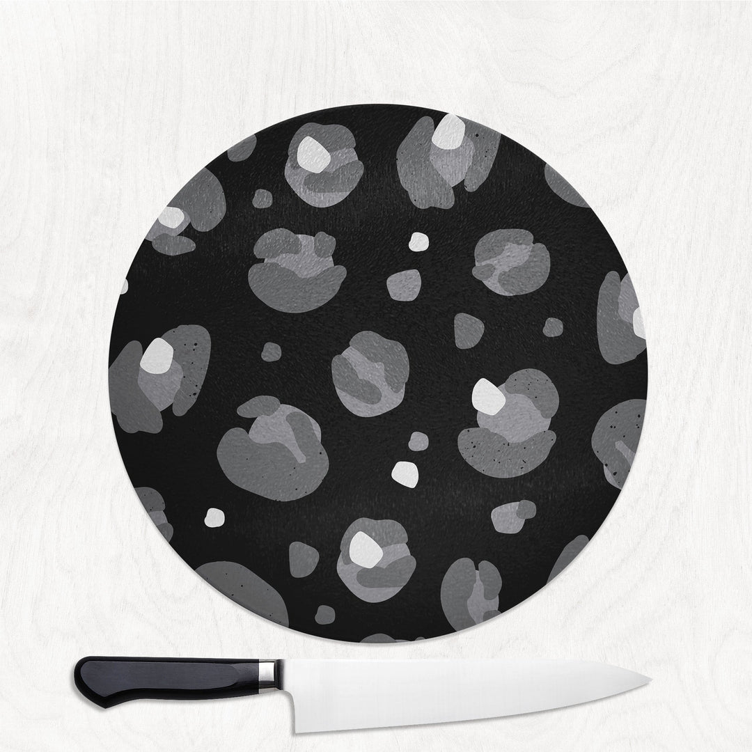 Round black cutting board with gray pattern and a knife on a white background