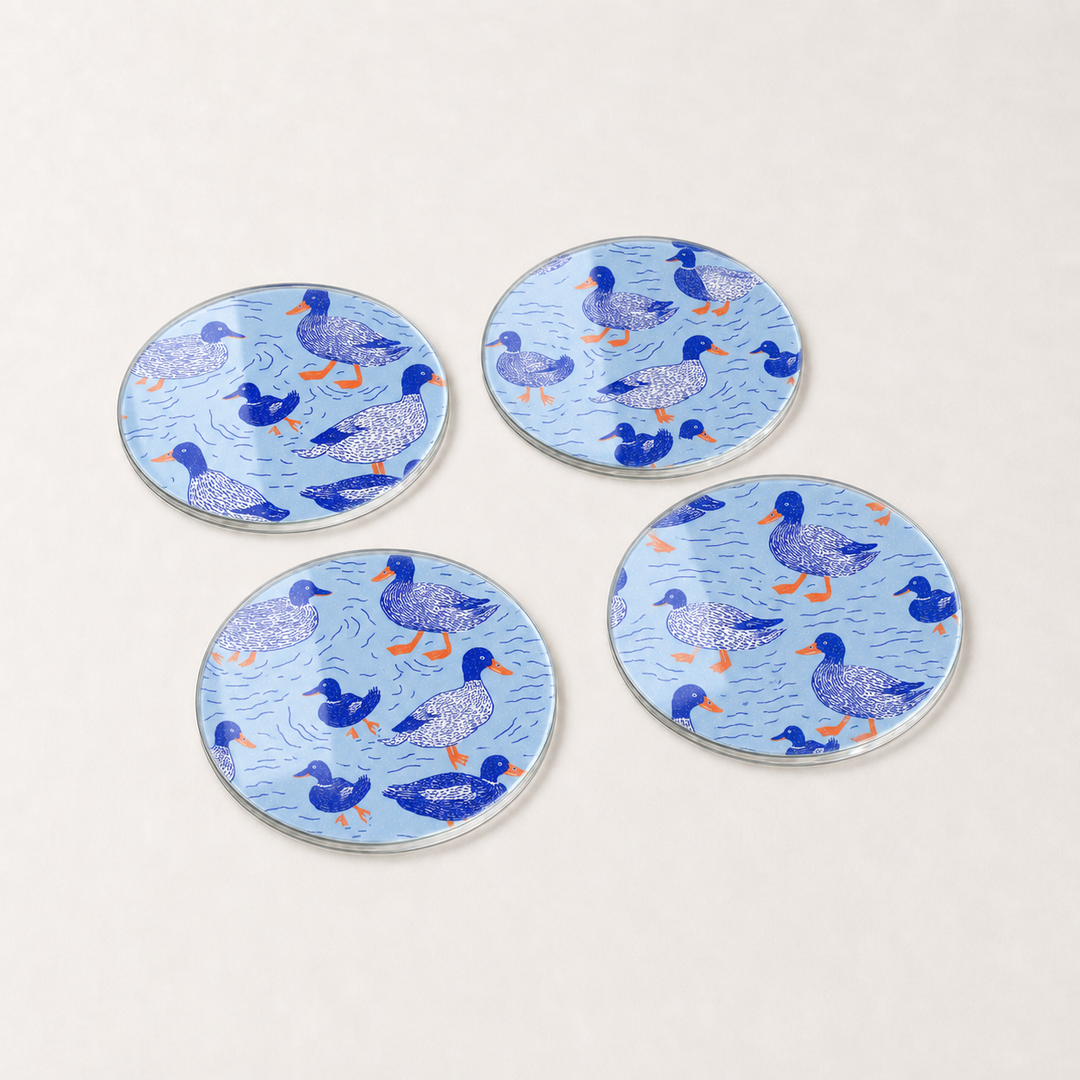 Four round blue glass coasters with duck pattern on a white background