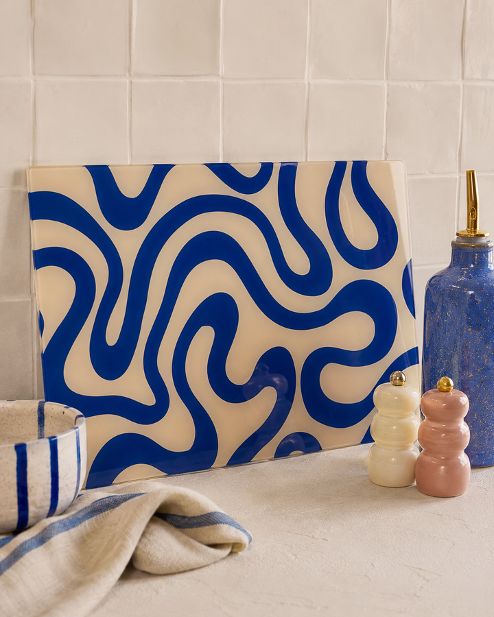 Decorative glass chopping glass board with blue wavy pattern in a kitchen setting leaned against a tiled wall