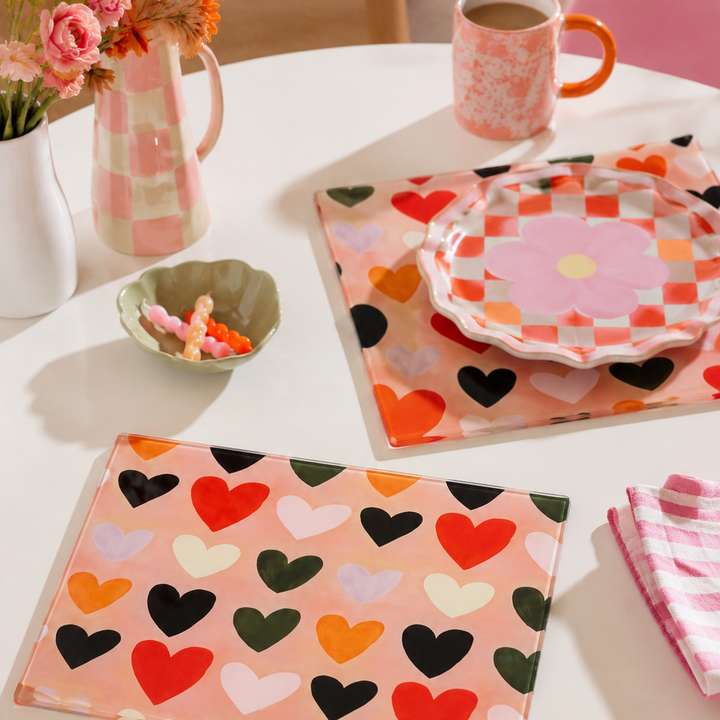 Table setting with boho heart-patterned glass placemats and napkins on a white table.