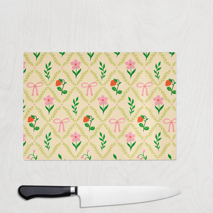 Glass chopping board featuring a green trellis pattern with pink bows and tiny flowers on a soft cream background.
