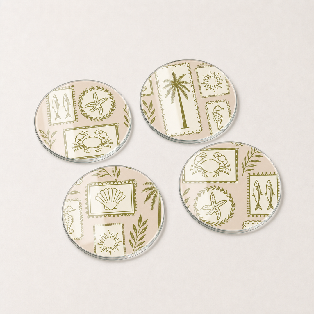 Four round glass coasters with beach-themed designs on a light gray background