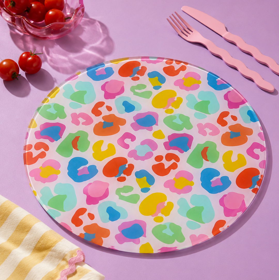 Colourful leopard print plate on a pink background with tomatoes, a fork, and knife.
