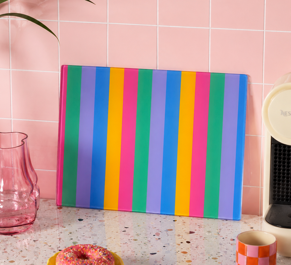 Colourful striped cutting board worktop saver on a kitchen counter with pink tiles in the background