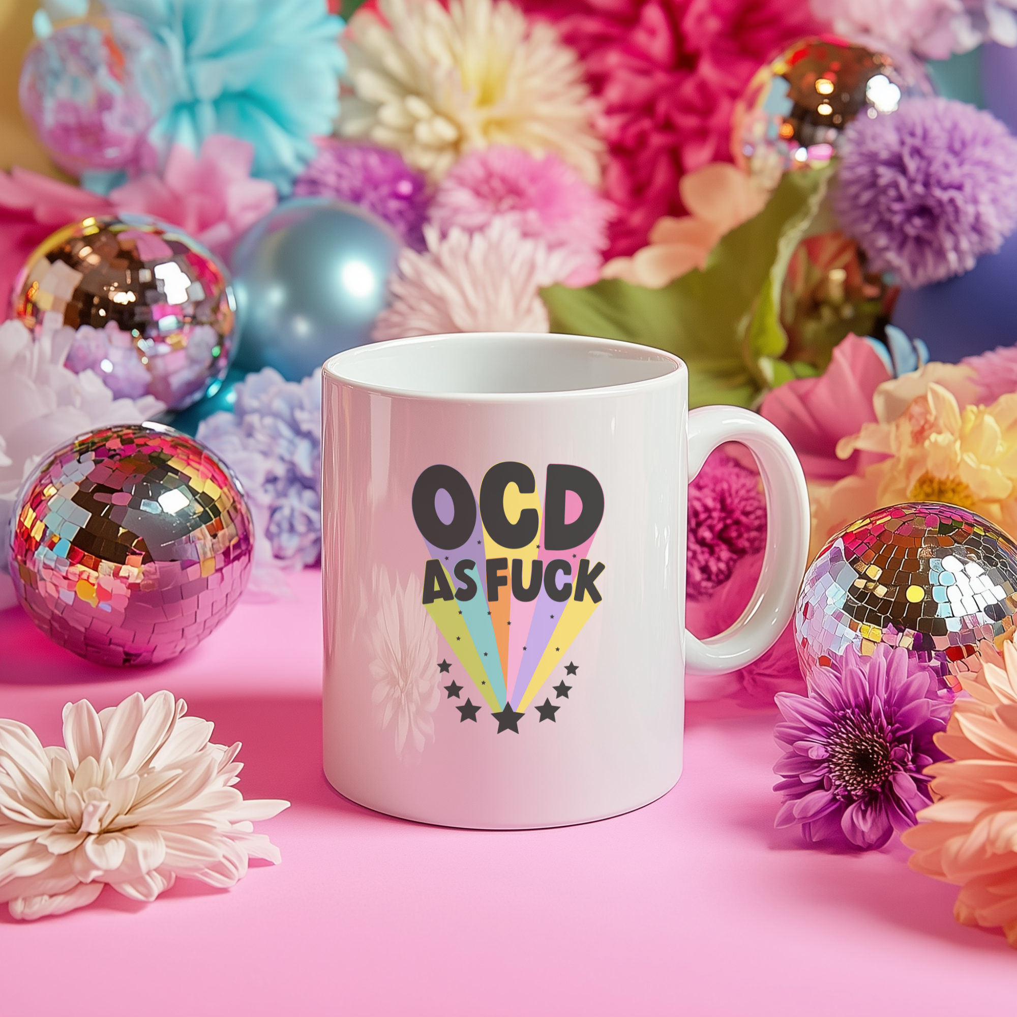 The Yililo OCD As Fuck Mug Cup is a bold, colorful statement mug with a heart handle, shown on a pink surface among bright artificial flowers and shiny disco balls.