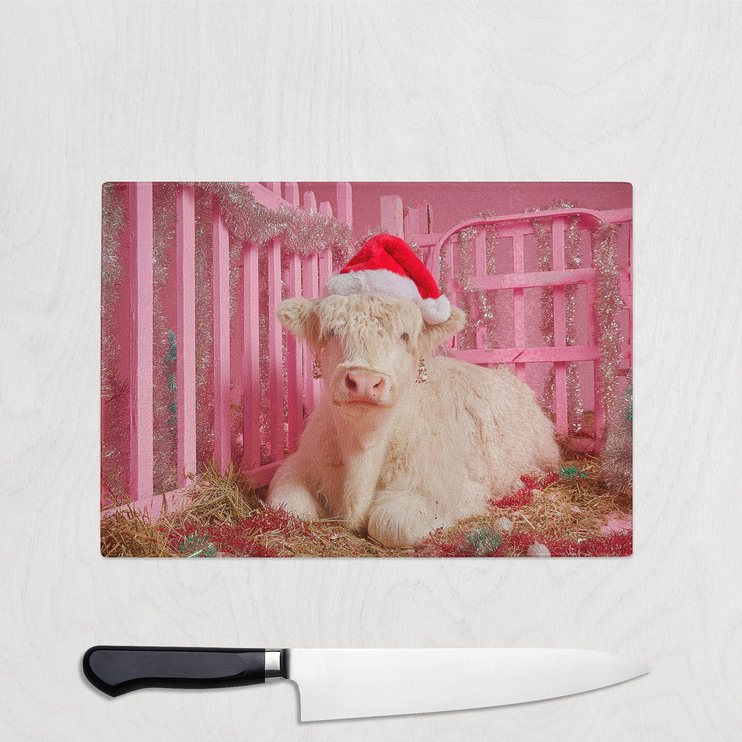 Calf wearing a Santa hat in front of a pink fence with a knife in the foreground.