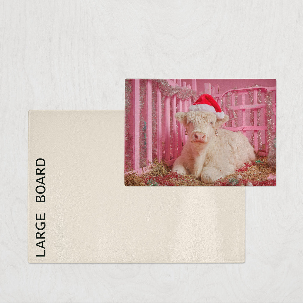 Large board with a photo of a calf in a pink pen wearing a Santa hat on a white background.
