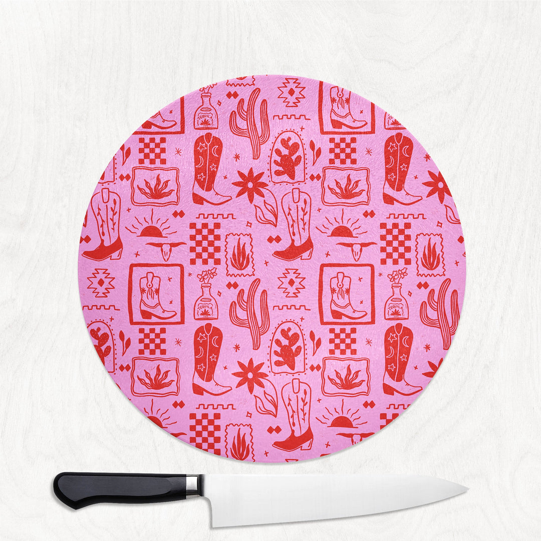 Round pink cutting board with cowboy pattern and a knife on a white background