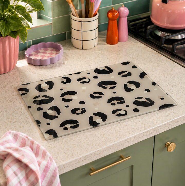 A rectangular glass cutting board with a black leopard print pattern, displayed on a speckled kitchen countertop.