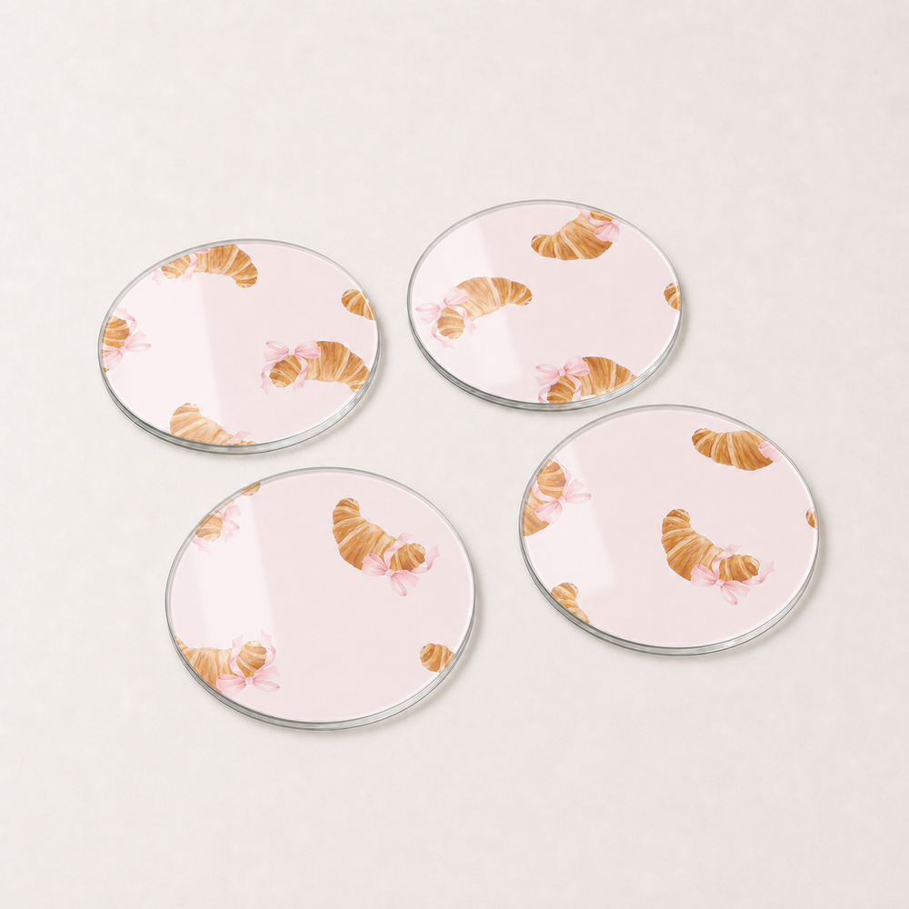 Four round ceramic coasters with croissant design on a light pink background