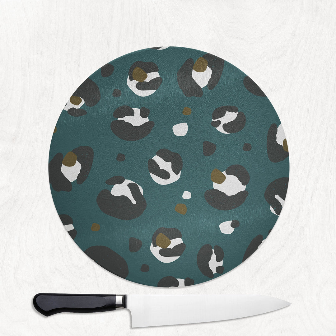 Round cutting board with a pattern of birds on a teal background, accompanied by a knife.