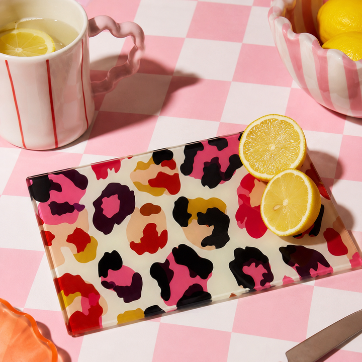 Colourful leopard print glass chopping board with lemons on a pink checkered tablecloth.
