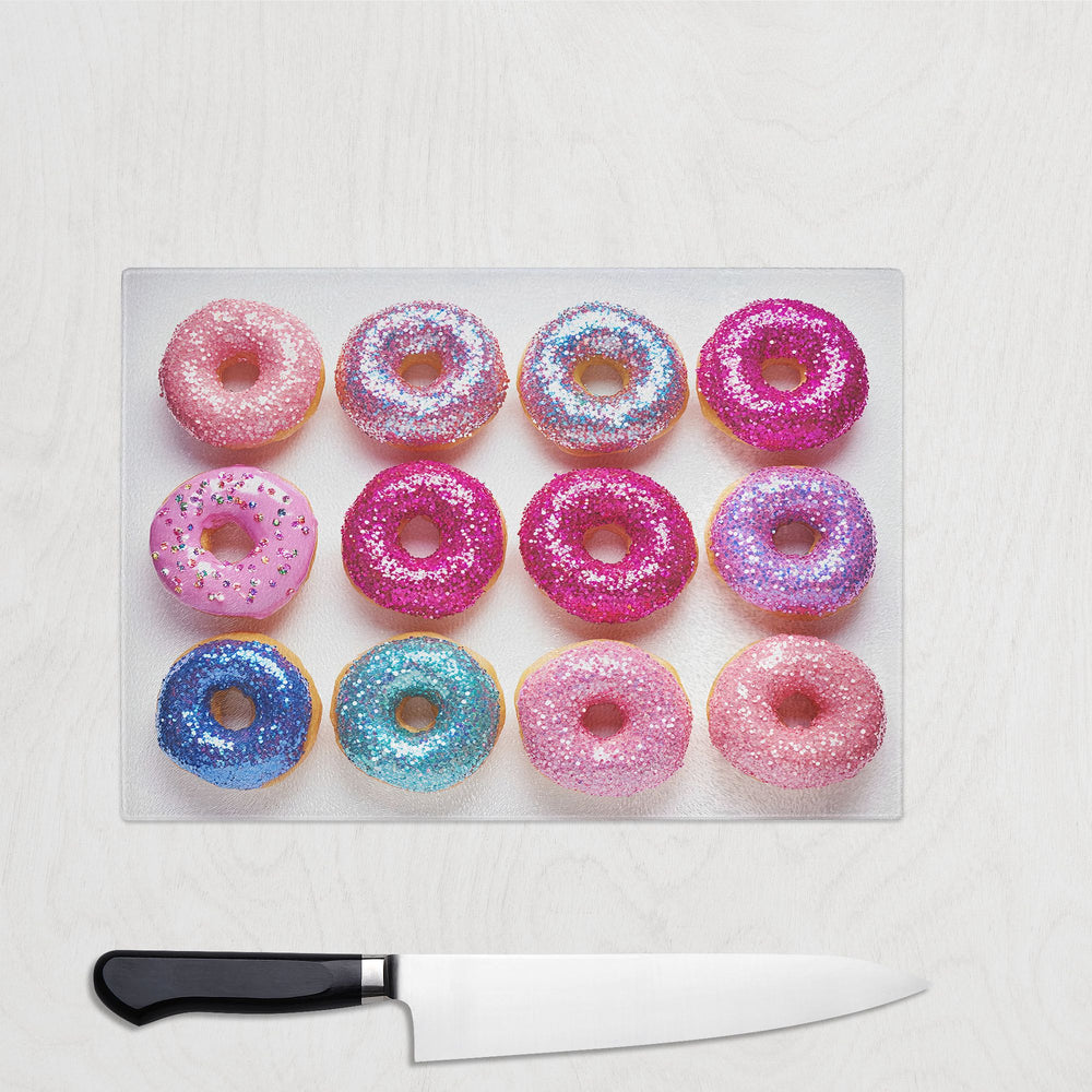The Yililo Glitter Doughnut Glass Chopping Board features twelve colorful doughnuts in neat rows, with a black-handled knife below, creating playful and vibrant kitchen decor on a light wood surface.
