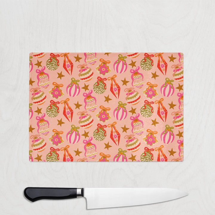 Glass cutting board with festive bauble design and a knife on a light gray background