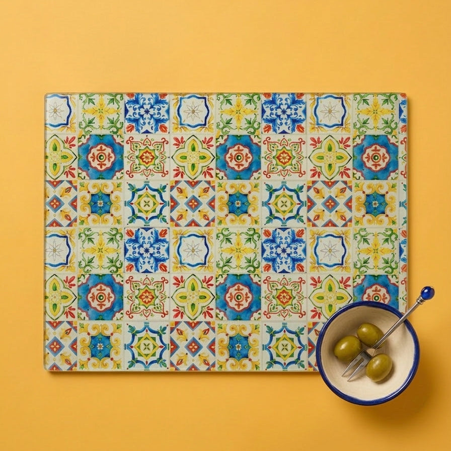 Colorful patterned glass chopping Board on a yellow background with a bowl of olives.