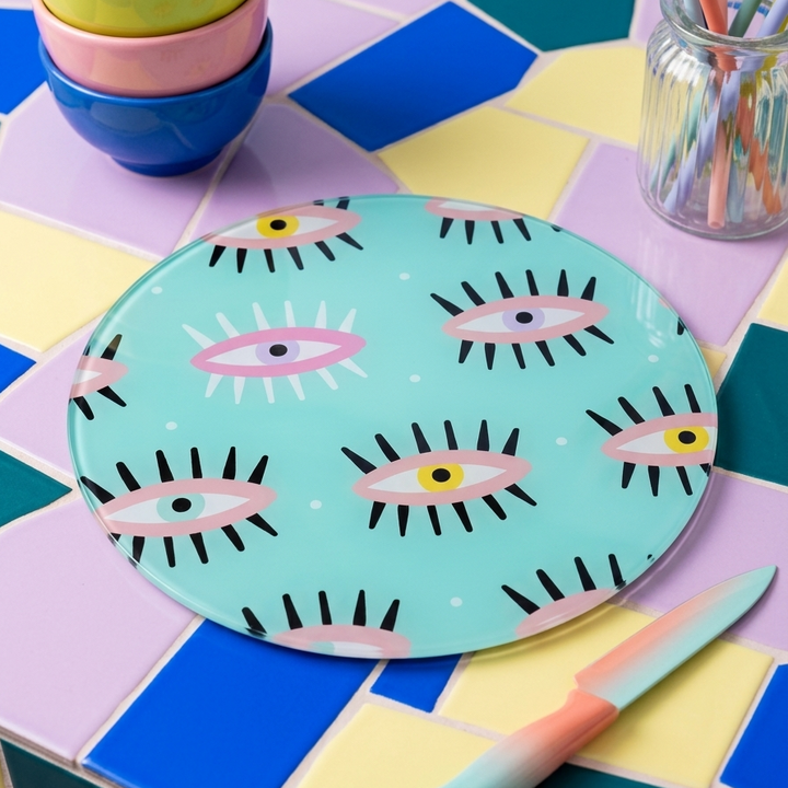 Round evil eye. Mint green glass chopping board with knife, bowls sitting on a tiled surface 