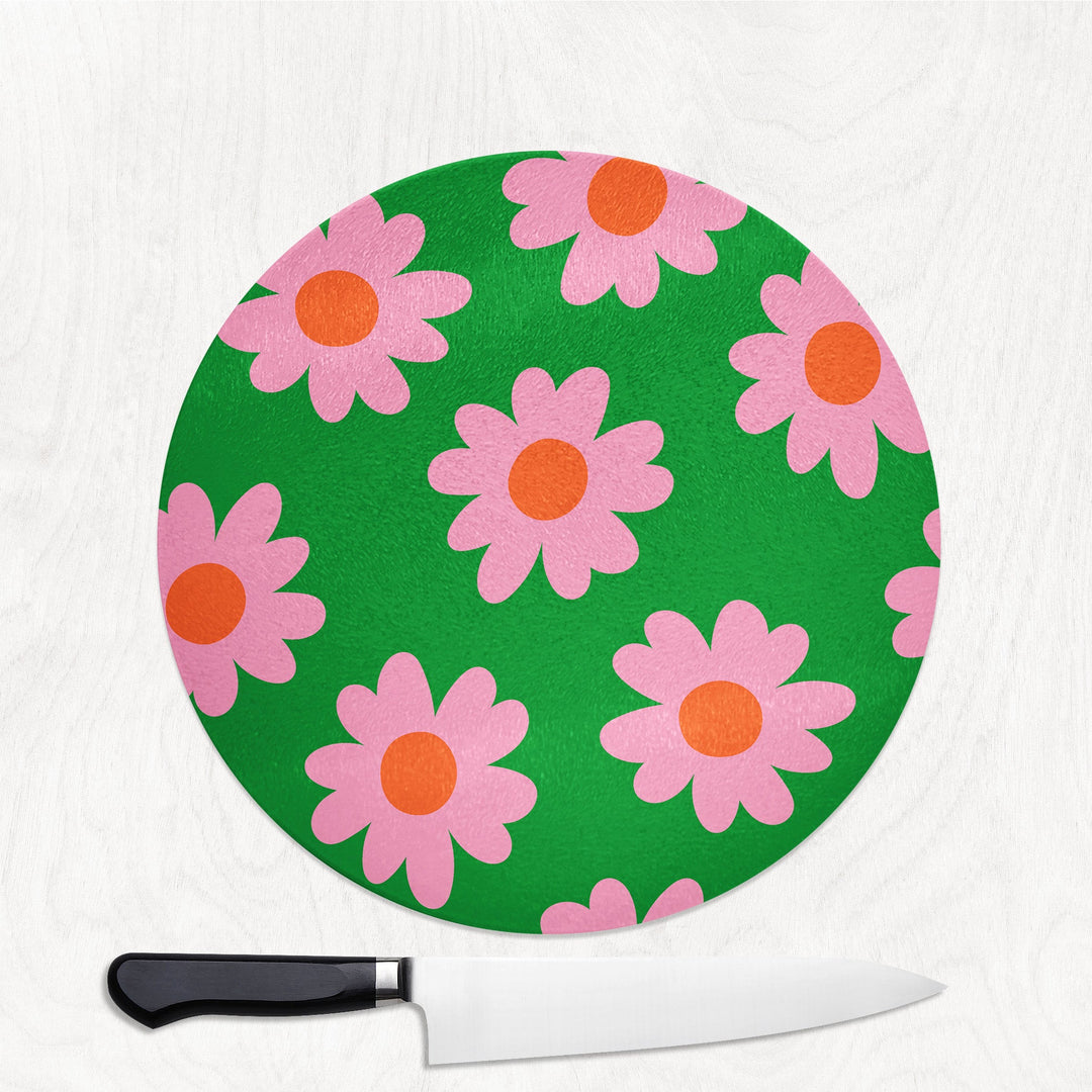 Round green cutting board with pink floral pattern and a knife on a white background