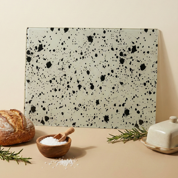 Ink Drop Black Speckled cream glass Chopping Board leaned against a wall with bread salt and rosemary sprigs and a butter dish
