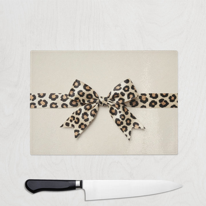 Leopard print bow chopping board with a knife below on a white background