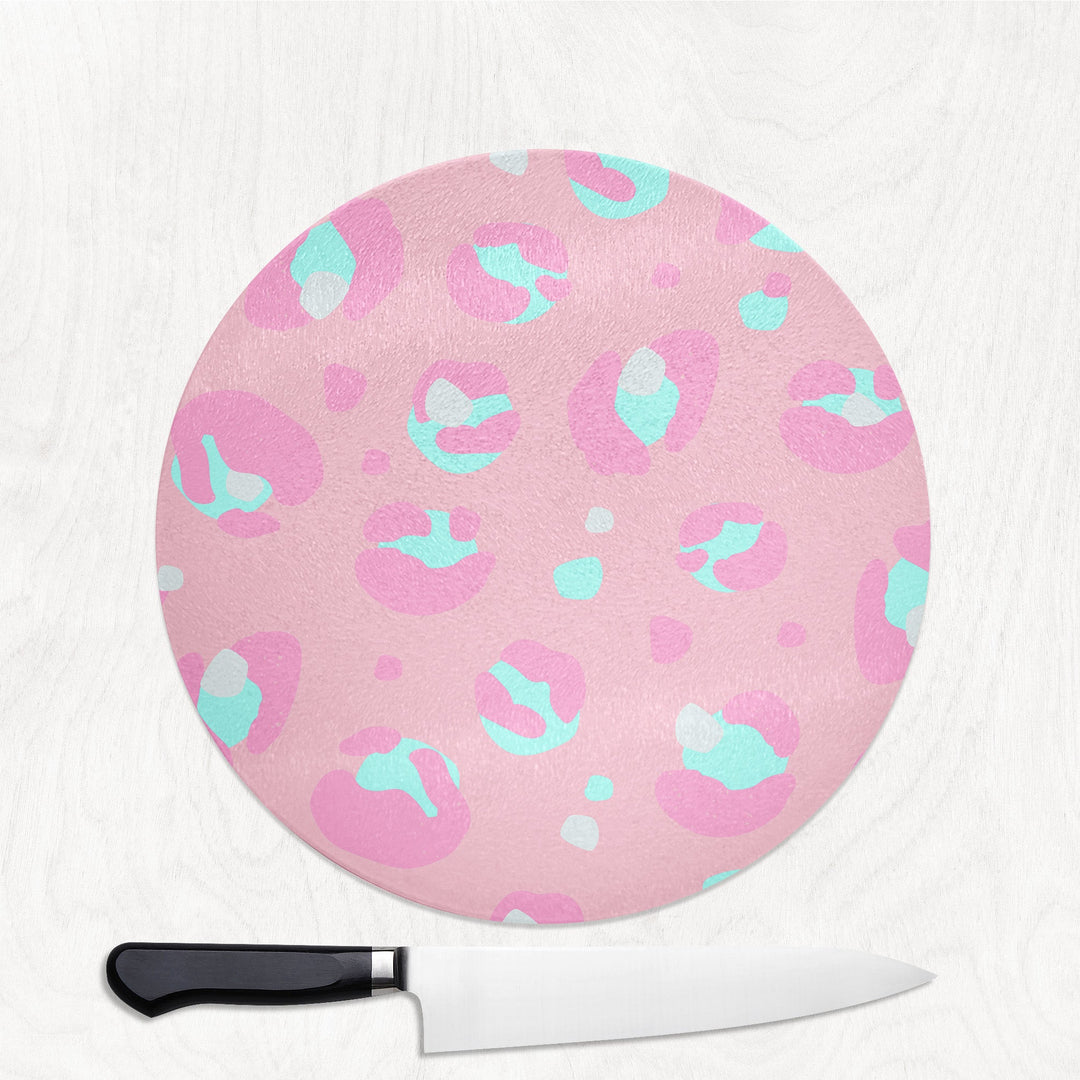 Round pink cutting board with blue and pink abstract patterns on a white background, accompanied by a knife.