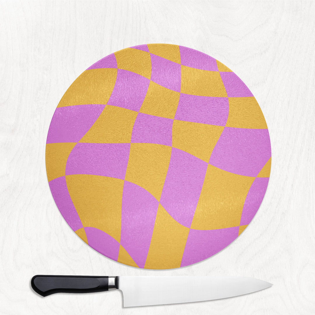 Round cutting board with purple and yellow checkered pattern on a white background