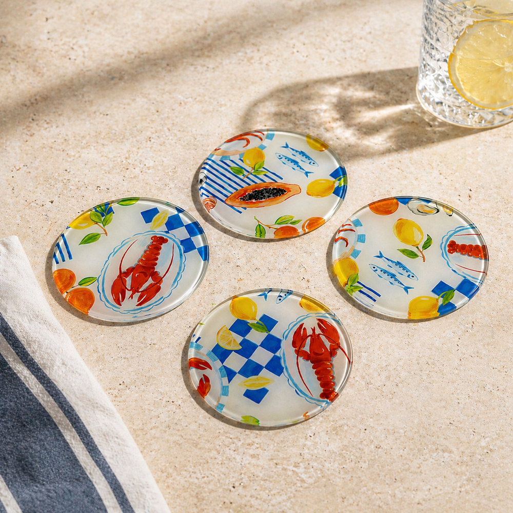 Set of four colorful coasters with marine-themed designs on a sandy surface.