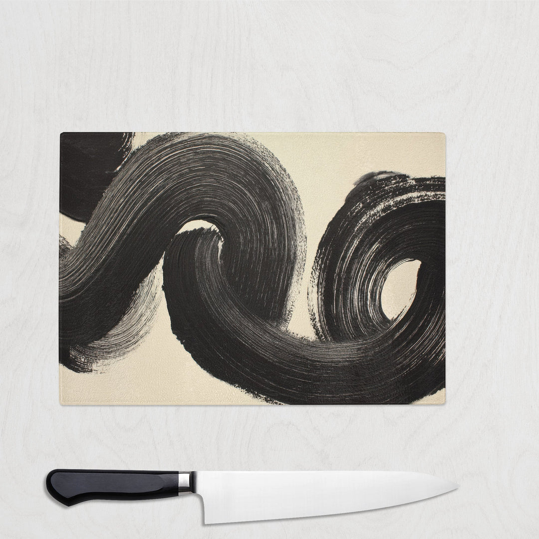 Monochrome glass chopping board featuring abstract black brushstroke swirl on neutral background