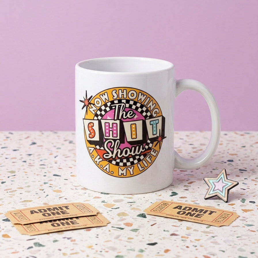Mug with colorful design and text on a terrazzo surface with tickets and a star-shaped object.
