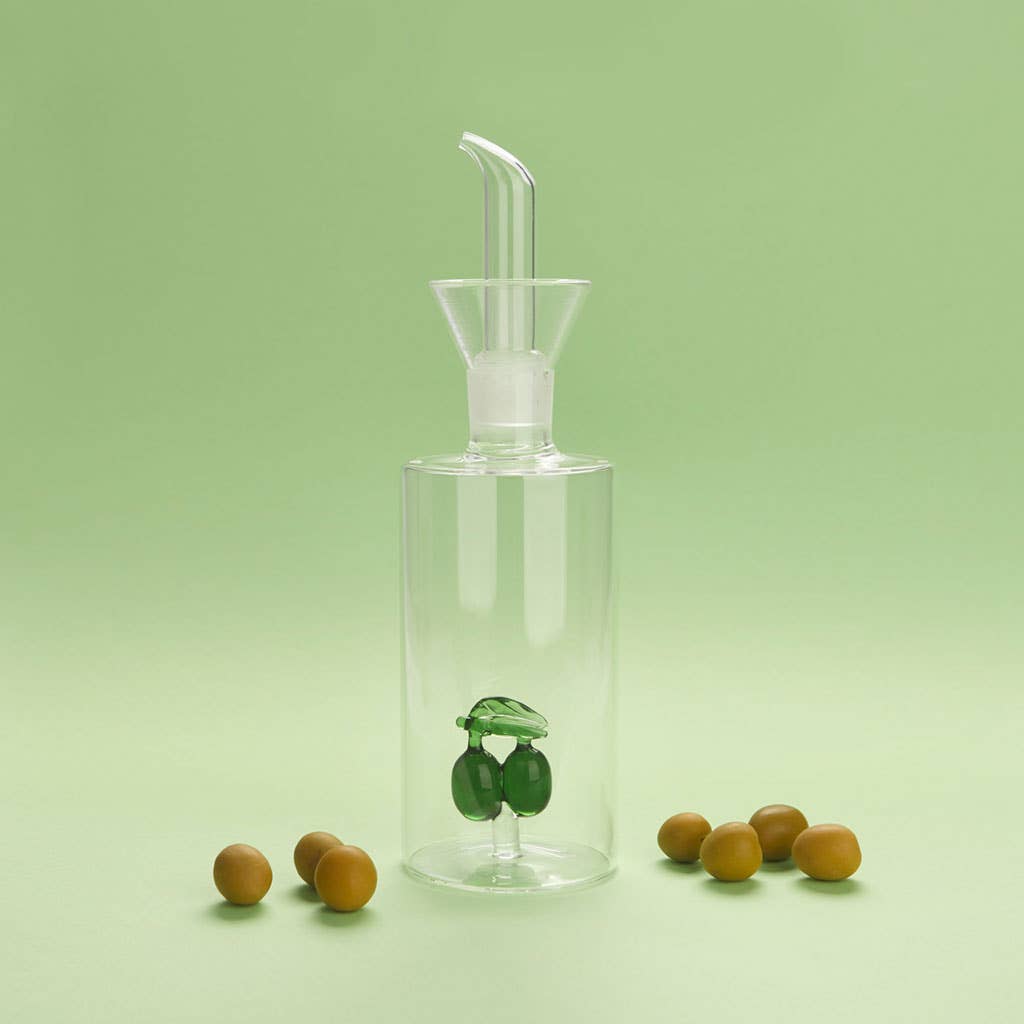 Clear glass olive oil dispenser with olives on a green background