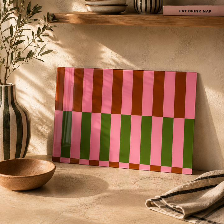 Pink and Green stripe glass worktop saver leaned up against a plaster wall 