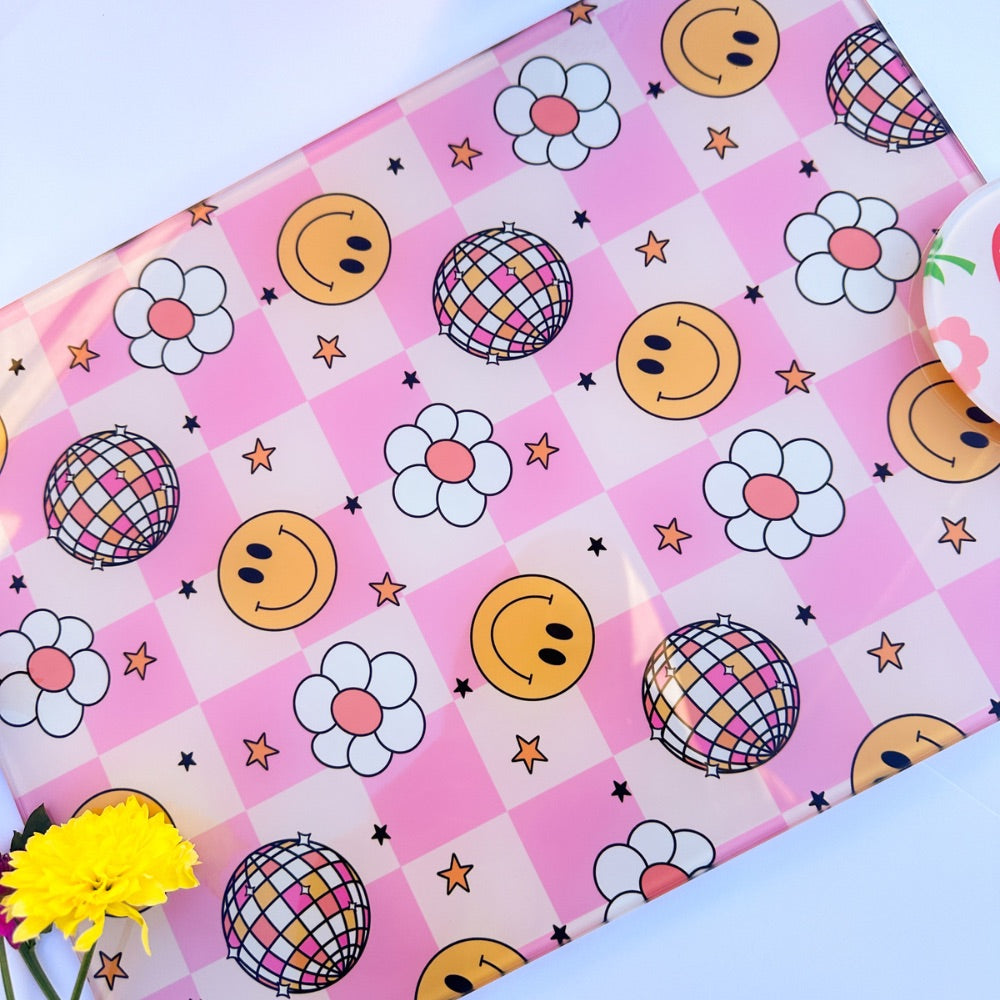 The Yililo Pink Smiley Disco Ball Glass Chopping Board adds retro charm with pink checks, yellow smiley faces, disco balls, black stars, and white flowers. A yellow flower decorates the bottom left corner for a playful touch.