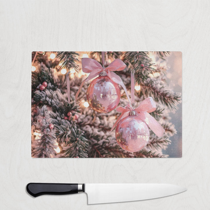 Decorative cutting board with Christmas-themed design featuring pink ornaments and tree branches on a white surface.
