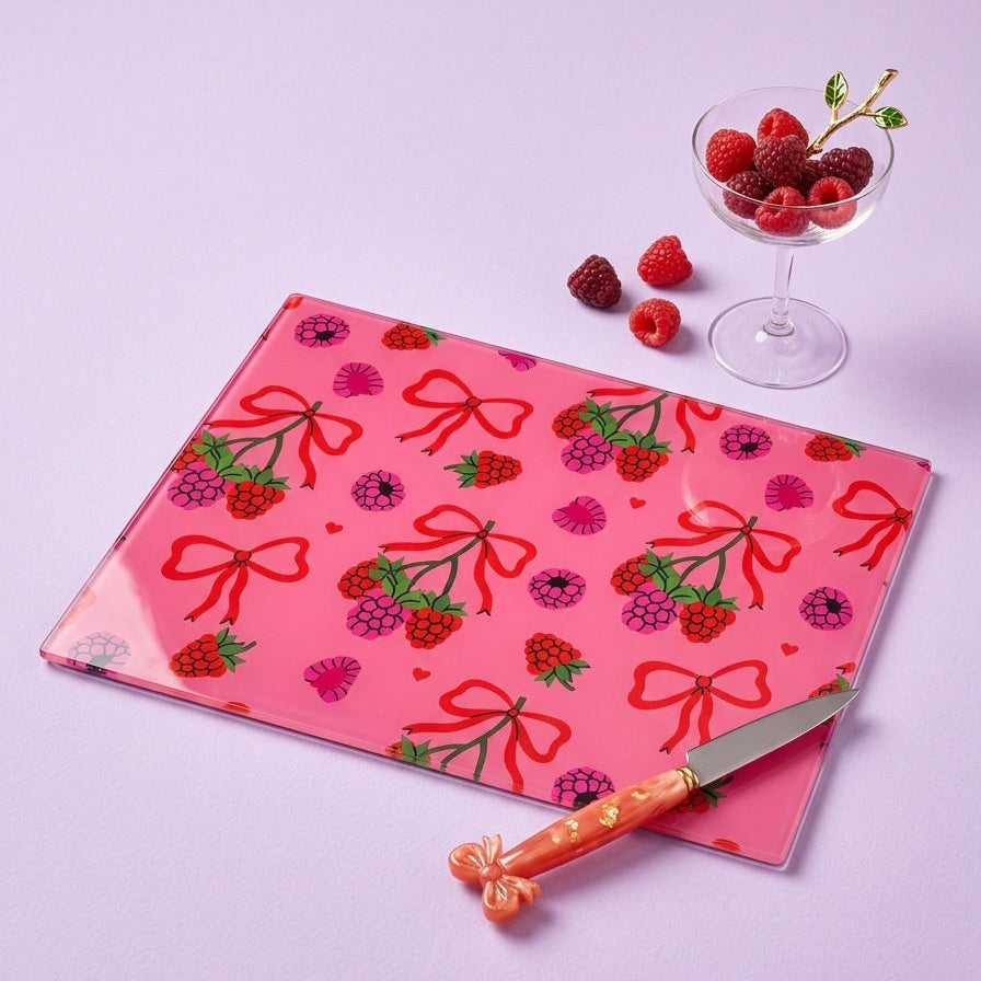 Pink cutting board with berry pattern, knife, and berries on a light purple background