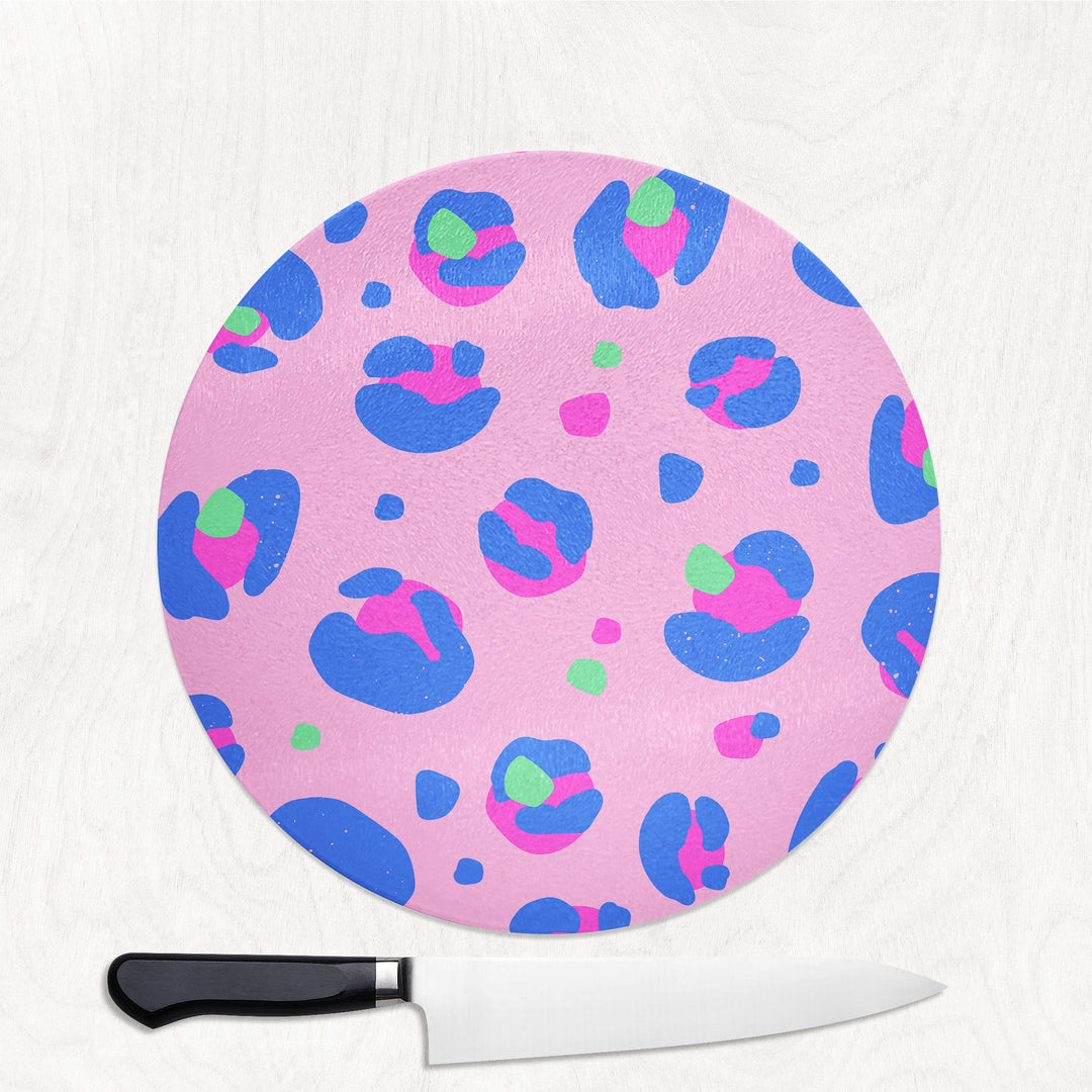Round pink cutting board with blue and green abstract patterns next to a knife on a white background