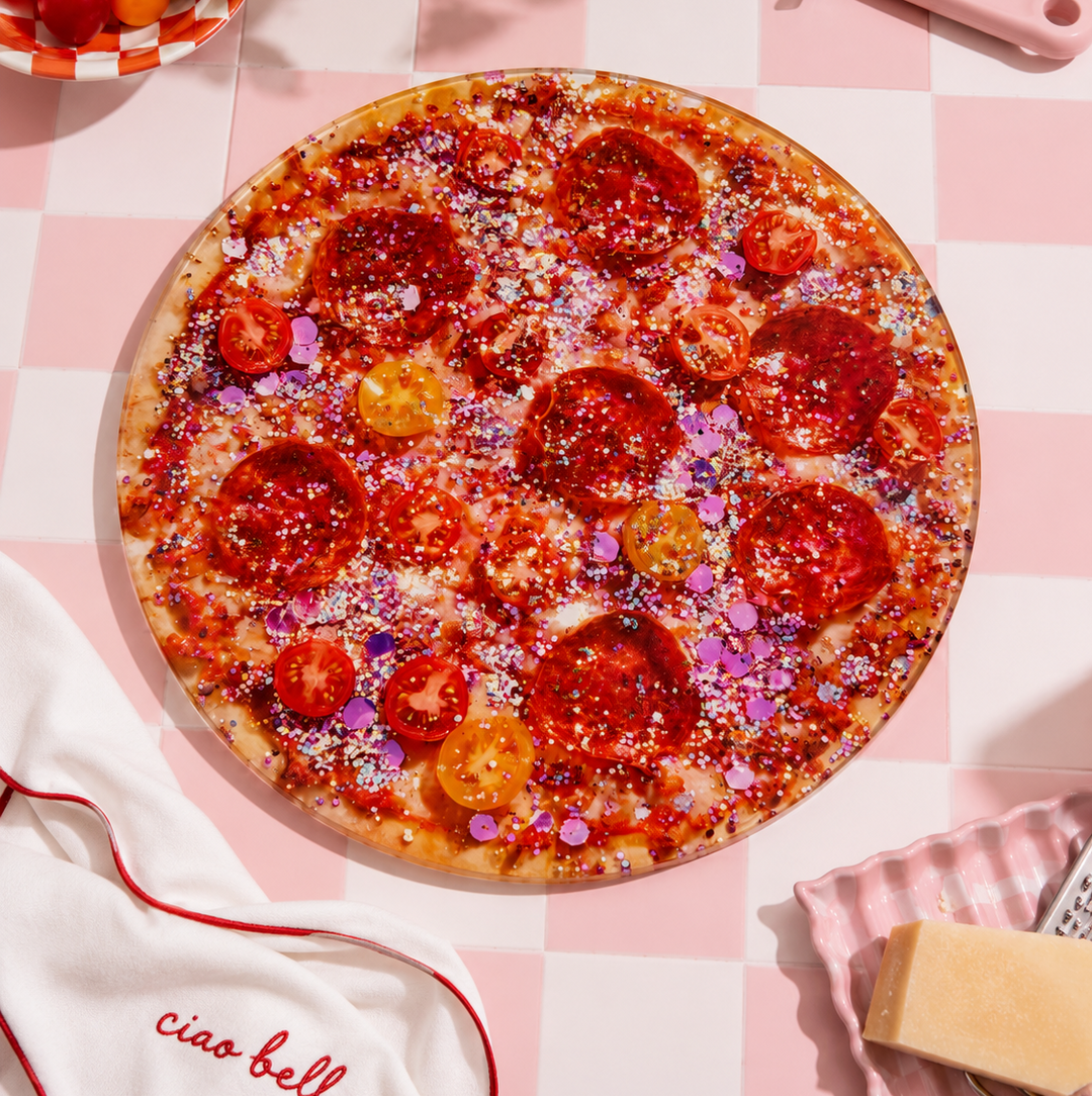 Pink glitter Pepperoni pizza style glass chopping board on a checkered tablecloth with a 'ciao bell' kitchen towel.