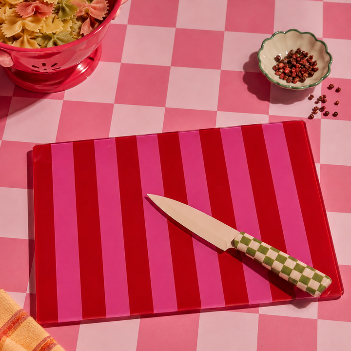 Red pink striped cutting board with a knife on a pink checkered tablecloth.