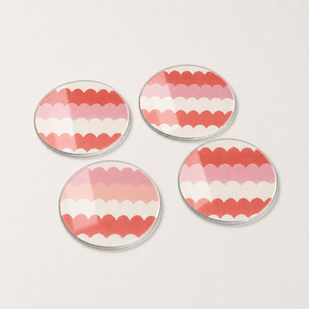 Four round glass coasters with pink and white scalloped pattern on a light gray background