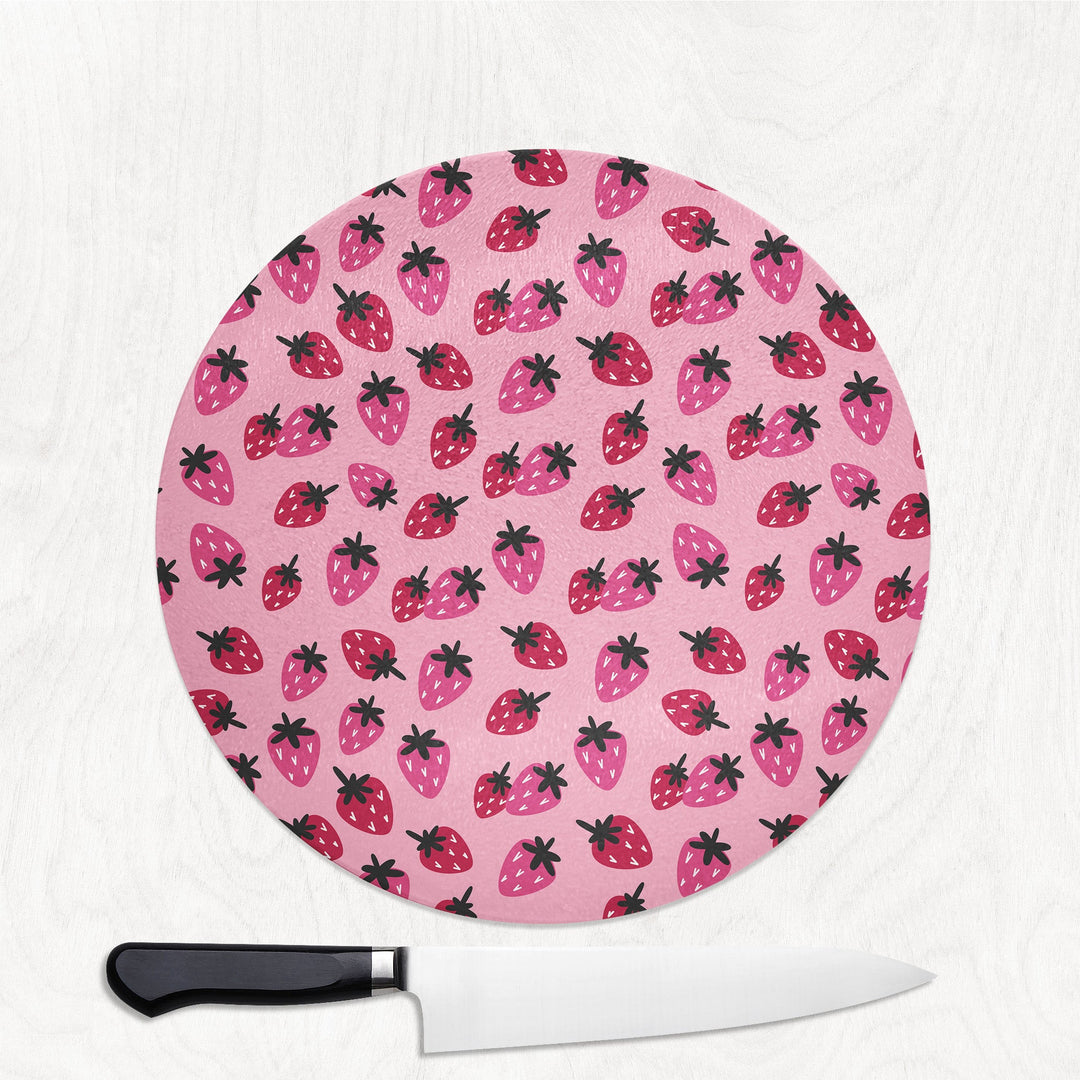 Round pink cutting board with strawberry pattern and a knife on a white background