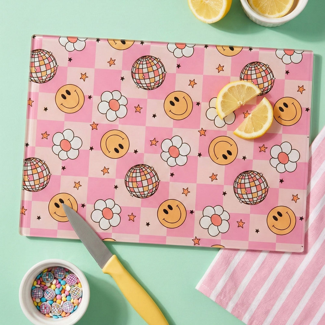 Pink cutting board worktop saver with smiley face and disco ball pattern on a green background