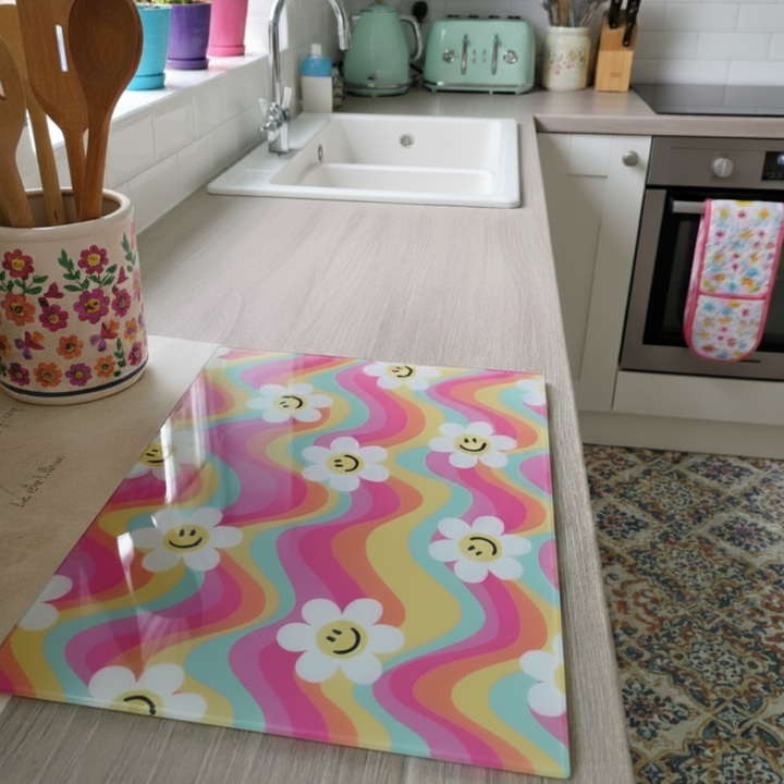 Colorful kitchen glass chopping board with smiley faces and flowers on a wooden surface.