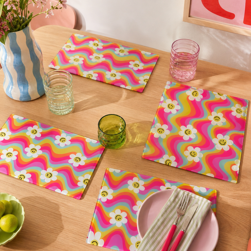 Colorful table setting with zigzag rainbow patterned glass placemats and napkins on a wooden table.
