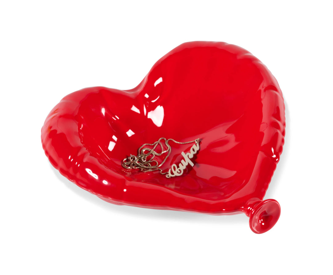 Red heart-shaped dish with a gold necklace on a white background