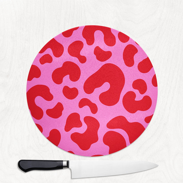 Round pink and red patterned cutting board with a knife on a white background