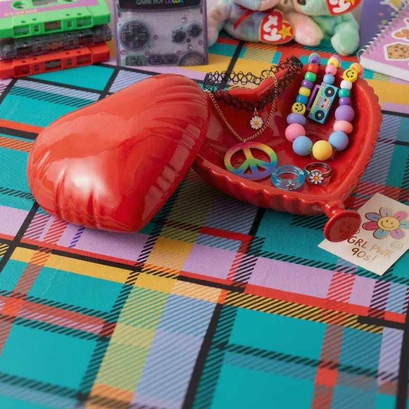 Red toy jewelry box with accessories on a colorful checkered tablecloth.