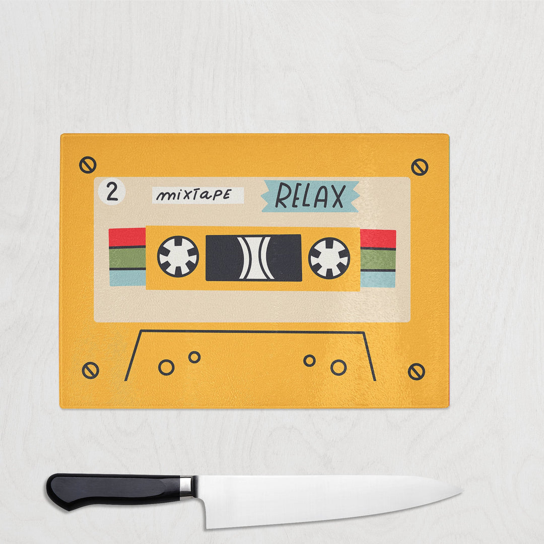 Yellow Relax Cassette Tape Style Glass Work Top Saver Chopping Board on a white background with a large knife